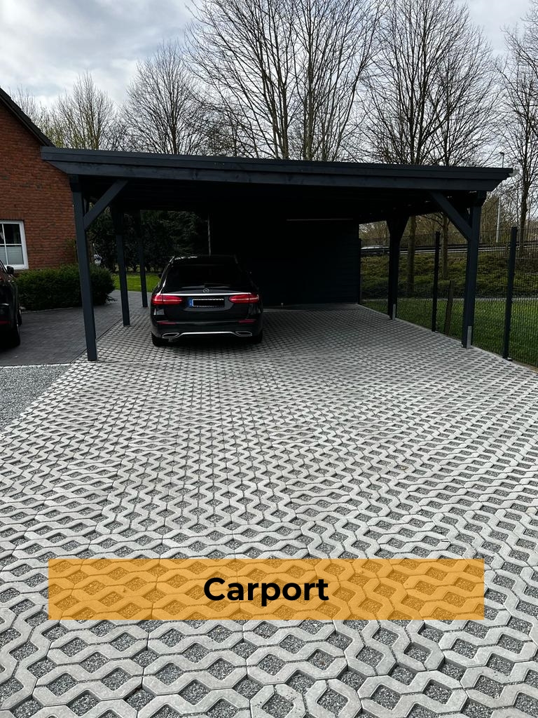 Ein freistehender, dunkelgrauer Doppelcarport aus Holz mit einem geparkten schwarzen Auto, davor eine breite Einfahrt aus Rasengittersteinen und im unteren Bereich ein orangefarbenes Banner mit dem Text „Carport“.