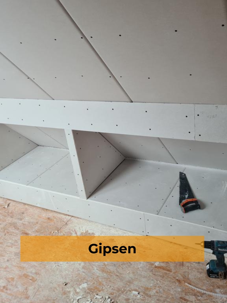Ein Innenbild, das eine Dachschräge zeigt, an der eine maßgefertigte Regaleinheit aus hellgrauen Gipsplatten montiert ist. Die Oberflächen der Regale und Wände sind mit zahlreichen schwarzen Schraubenpunkten übersät. Ein schwarzer Akku-Schrauber liegt auf der Holzboden, neben einem kleinen orange-schwarzen Handwerkzeug, im Vordergrund links. Ein orangefarbenes Banner im unteren Drittel des Bildes enthält den schwarzen Text "Gipsen".